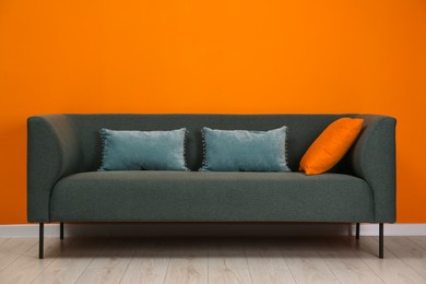 Photo of Stylish sofa with pillows near orange wall indoors