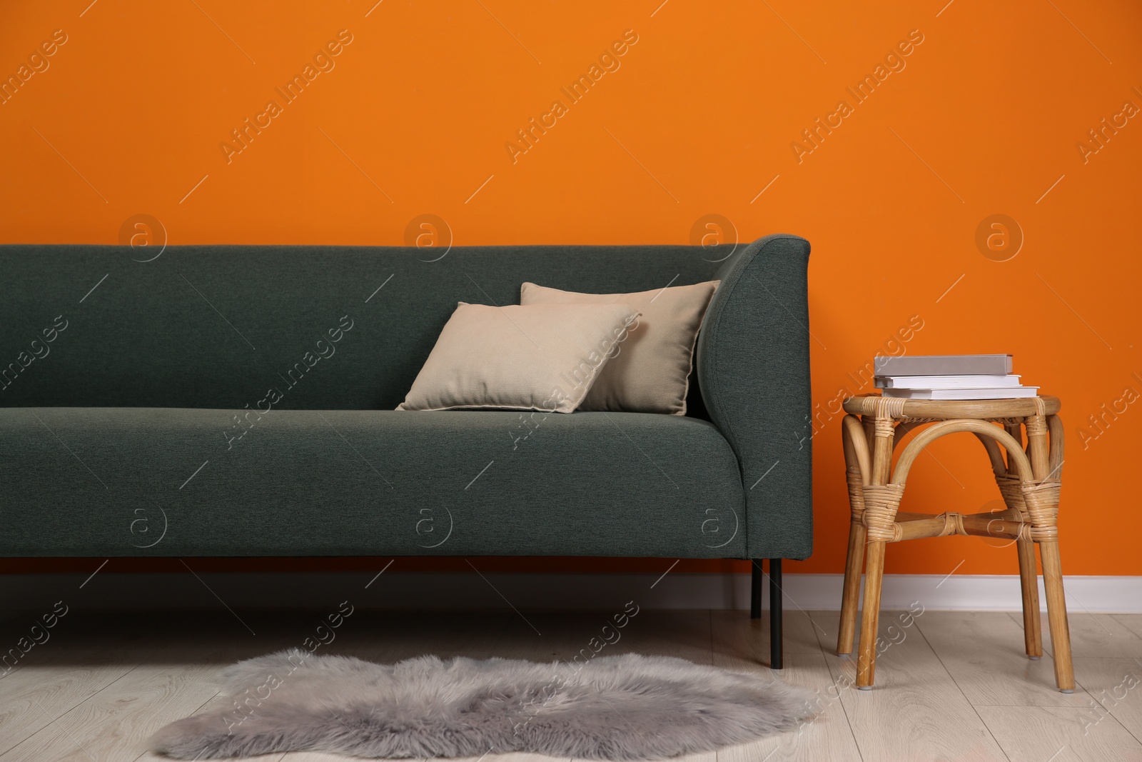 Photo of Stylish sofa with pillows and side table near orange wall indoors