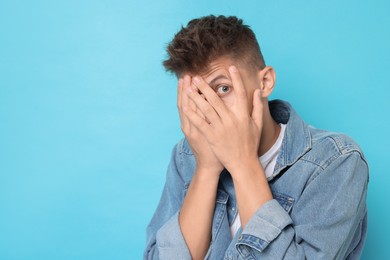 Portrait of scared young man on light blue background, space for text