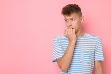 Portrait of scared young man on pink background, space for text