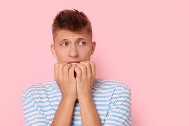 Portrait of scared young man on pink background, space for text