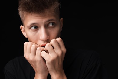 Portrait of scared young man on black background, space for text