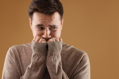 Portrait of scared young man on brown background, space for text