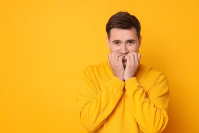 Portrait of scared young man on orange background, space for text