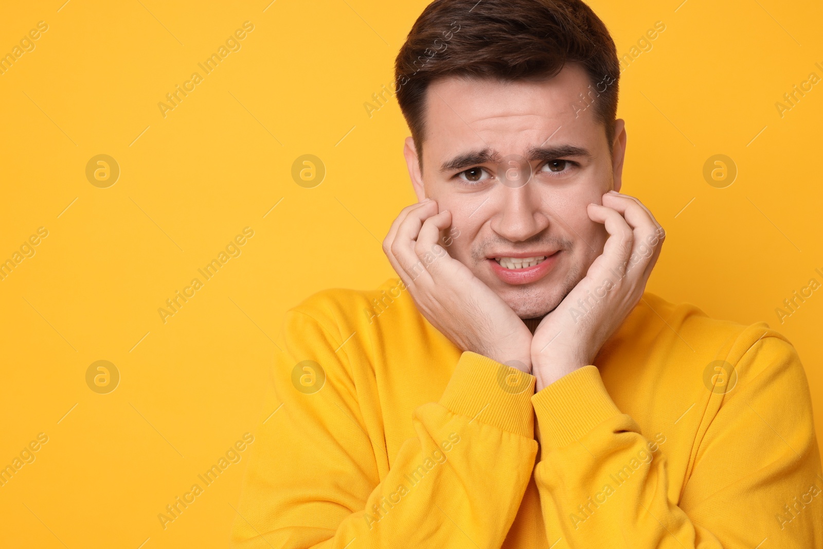 Photo of Portrait of scared young man on orange background, space for text