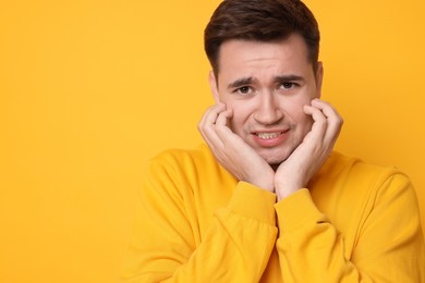 Photo of Portrait of scared young man on orange background, space for text