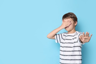 Photo of Scared little boy covering eyes on light blue background. Space for text