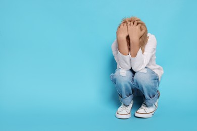 Photo of Scared little boy hiding on light blue background. Space for text