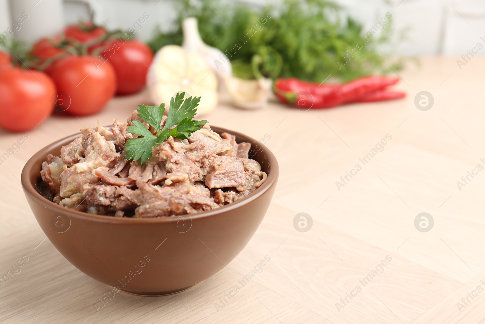 Photo of Canned meat with parsley in bowl on wooden table, closeup. Space for text