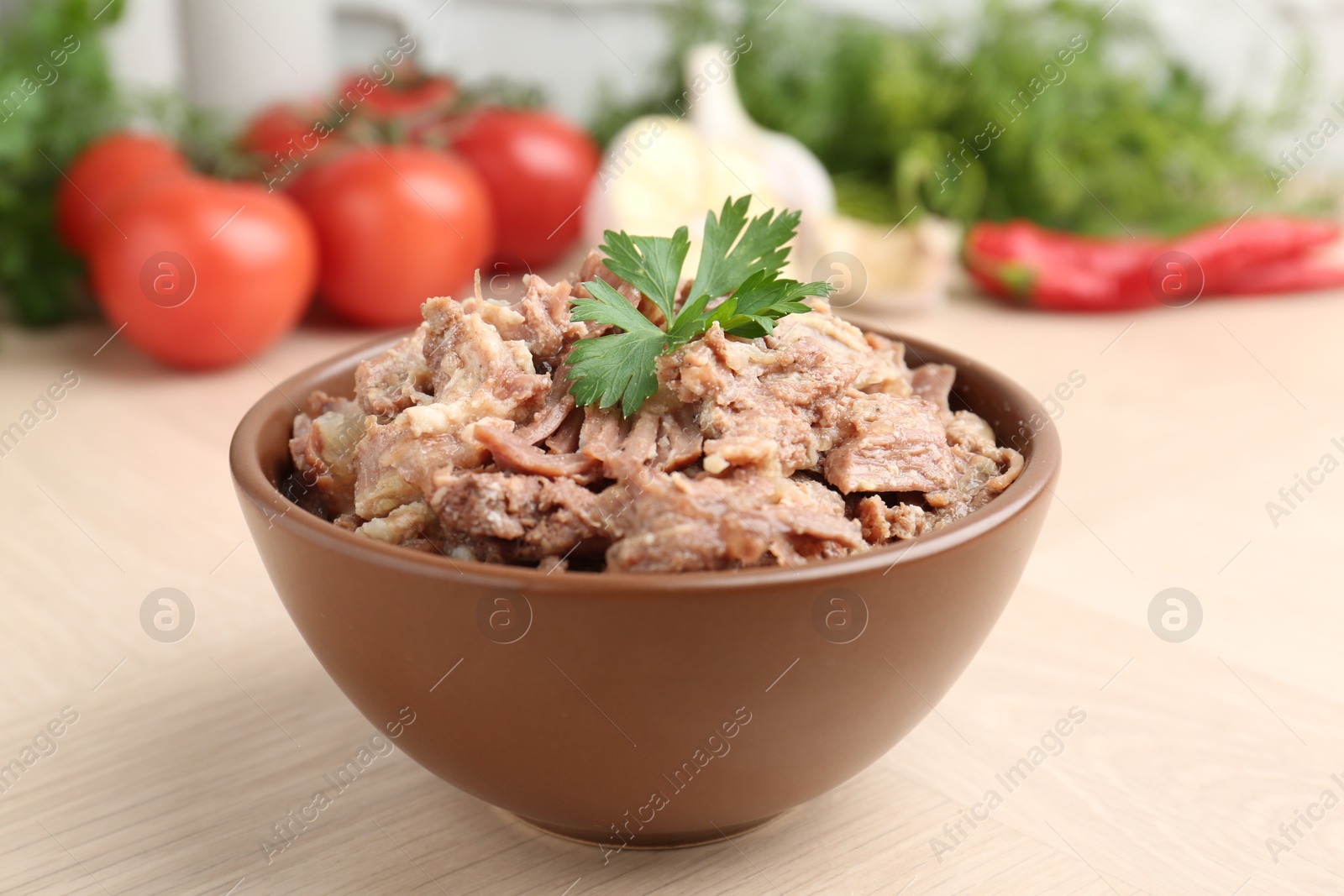 Photo of Canned meat with parsley in bowl on wooden table, closeup