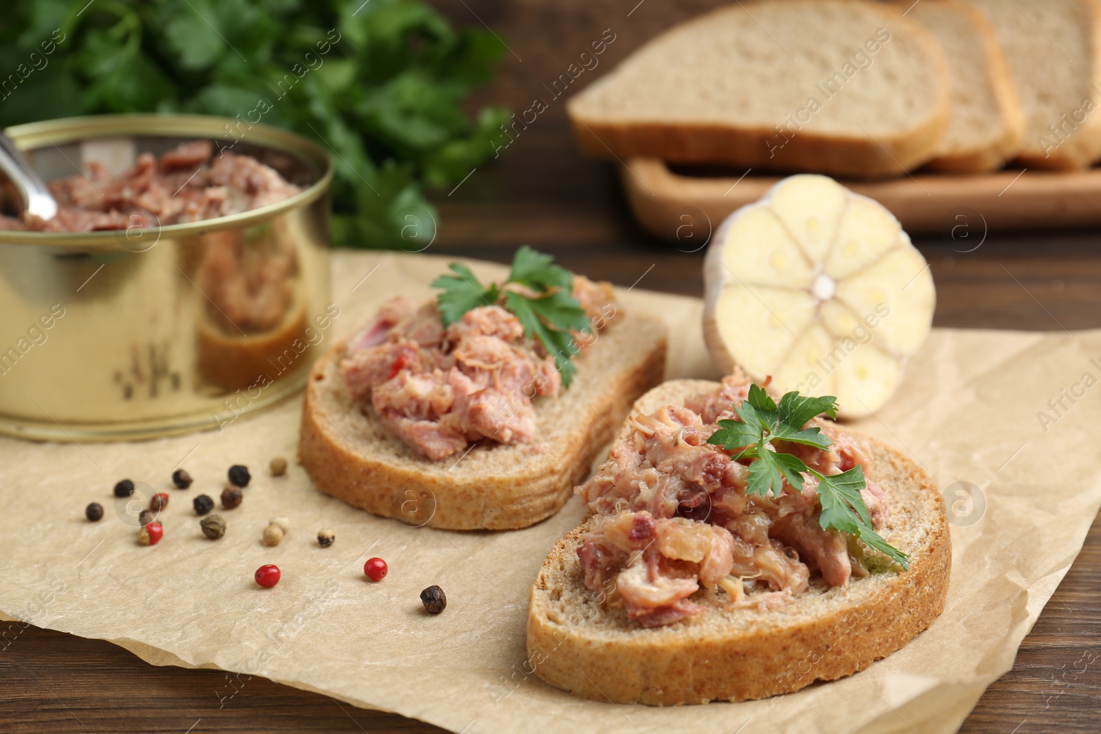 Photo of Sandwiches with canned meat, parsley, garlic and peppercorns on wooden table, closeup