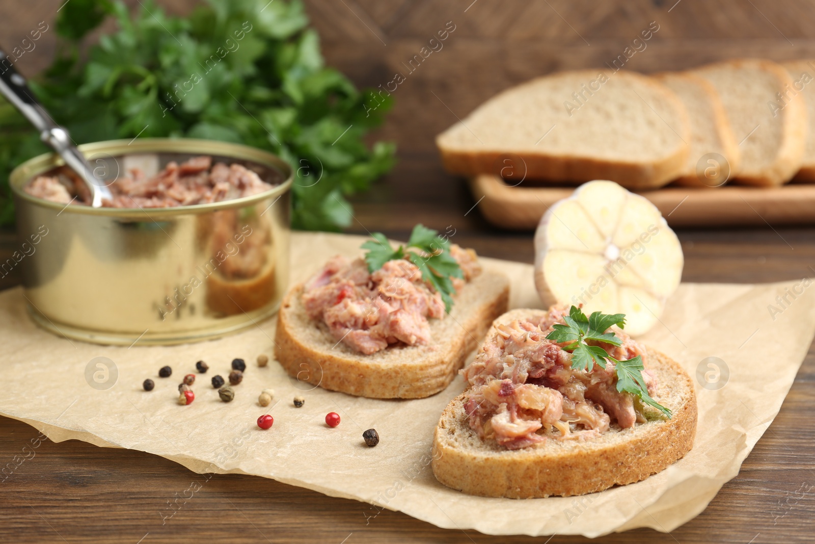 Photo of Sandwiches with canned meat, parsley, garlic and peppercorns on wooden table, closeup