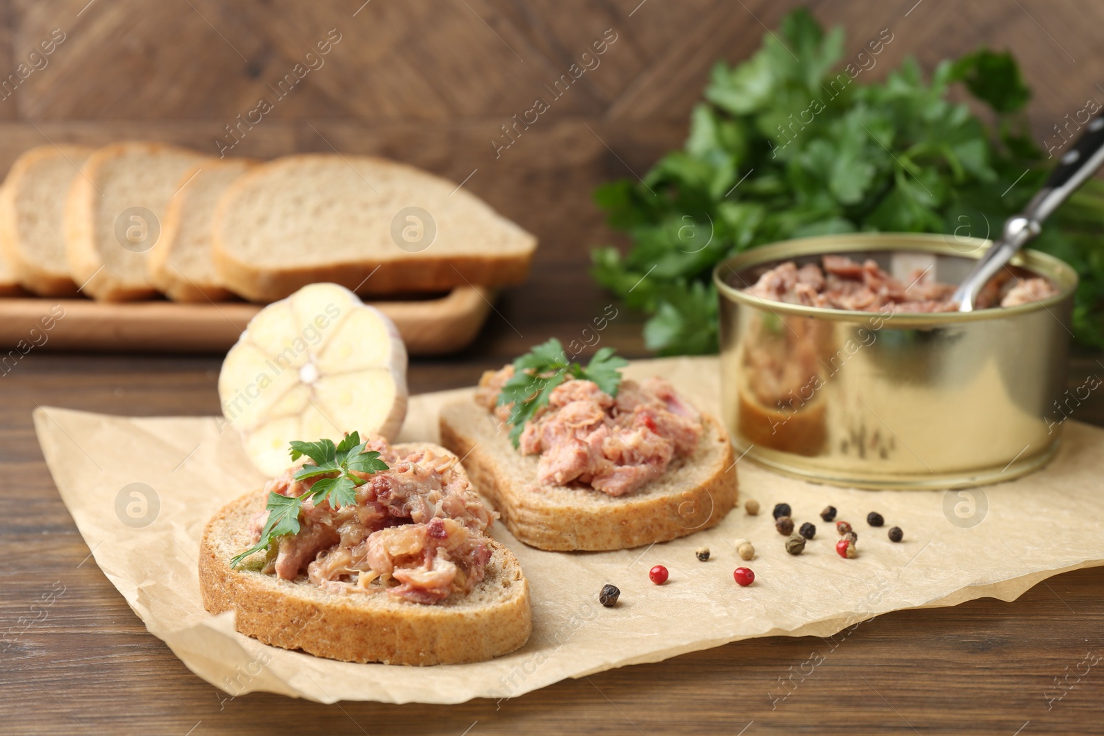 Photo of Sandwiches with canned meat, parsley, garlic and peppercorns on wooden table, closeup