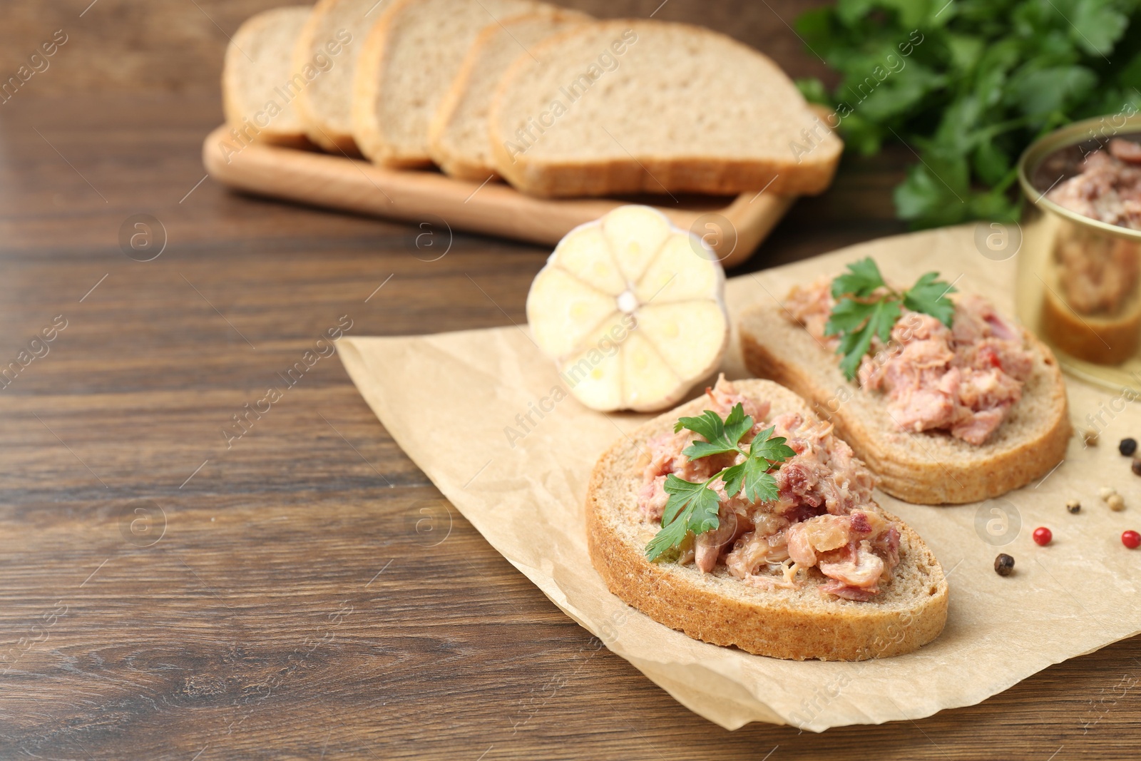 Photo of Sandwiches with canned meat, parsley, garlic and peppercorns on wooden table, closeup. Space for text