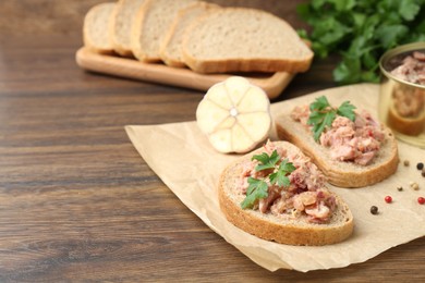 Photo of Sandwiches with canned meat, parsley, garlic and peppercorns on wooden table, closeup. Space for text