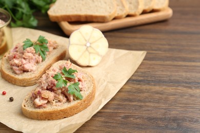 Sandwiches with canned meat, parsley and garlic on wooden table, closeup. Space for text