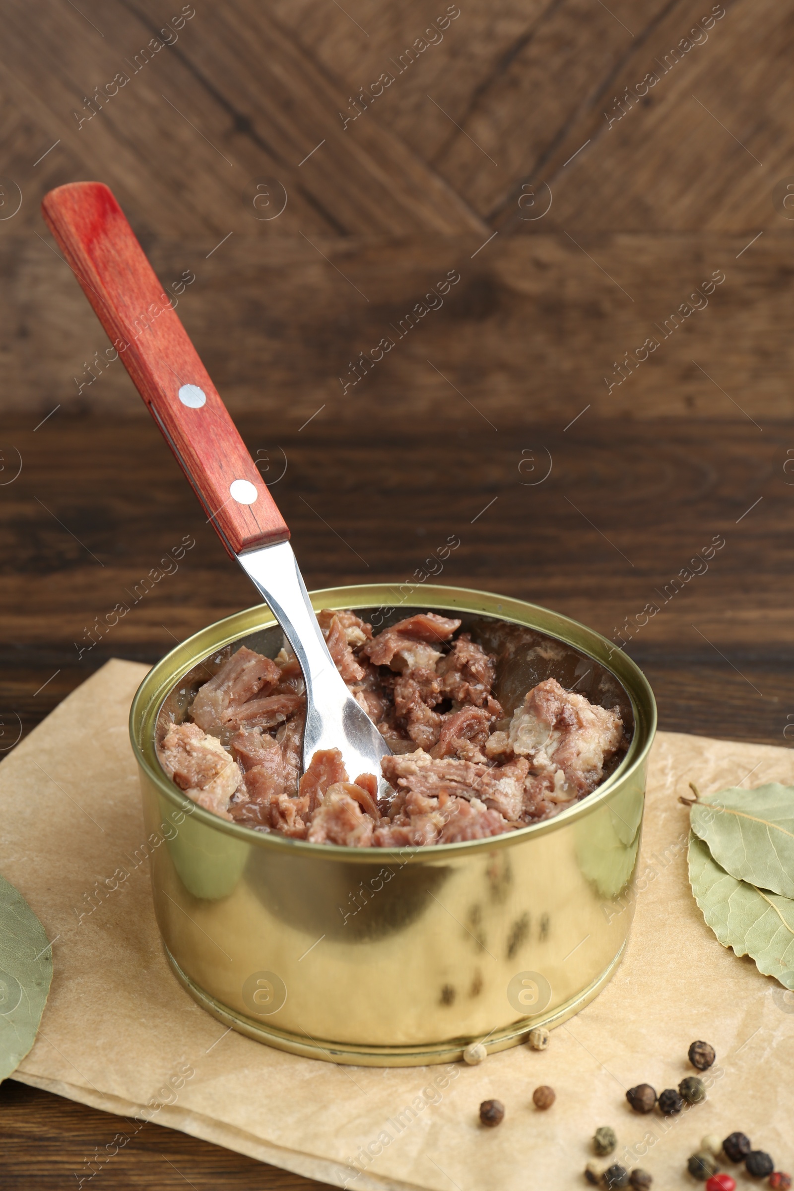 Photo of Canned meat in tin can on wooden table, closeup