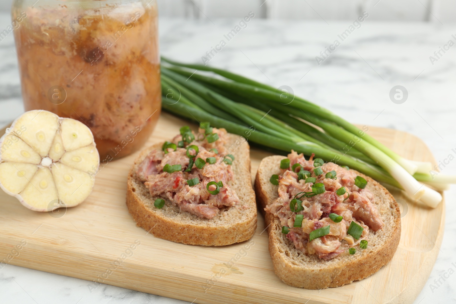 Photo of Sandwiches with canned meat and green onions on white marble table, closeup