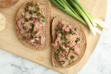 Photo of Sandwiches with canned meat and green onions on white marble table, top view