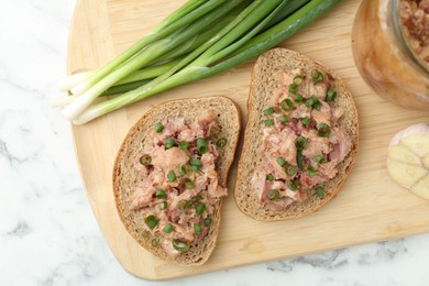 Photo of Sandwiches with canned meat and green onions on white marble table, top view