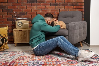 Man petting cute ginger cat at home