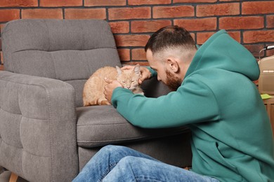 Man petting cute ginger cat at home