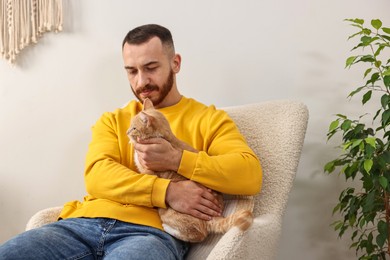 Man petting cute ginger cat on armchair at home