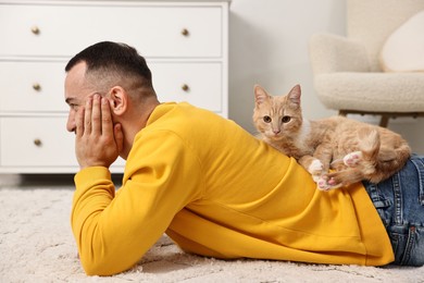 Man with cute ginger cat lying on floor at home