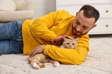 Man petting cute ginger cat on floor at home