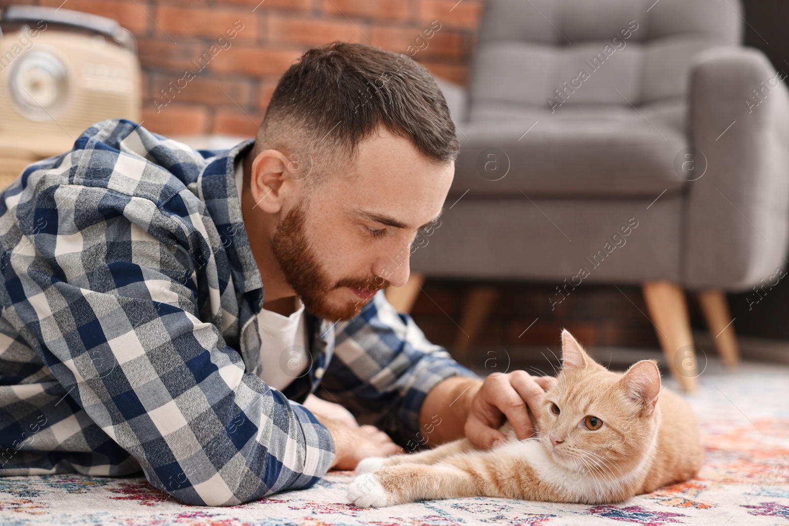 Photo of Man petting cute ginger cat on floor at home