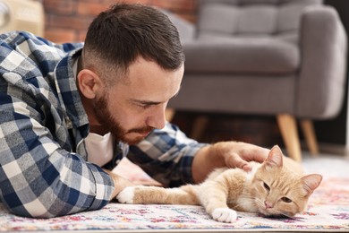 Man petting cute ginger cat on floor at home