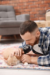 Man petting cute ginger cat on floor at home