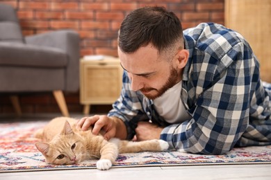 Photo of Man petting cute ginger cat on floor at home