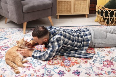 Man petting cute ginger cat on floor at home