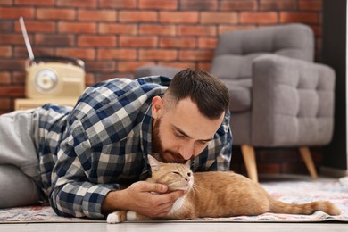 Man petting cute ginger cat on floor at home