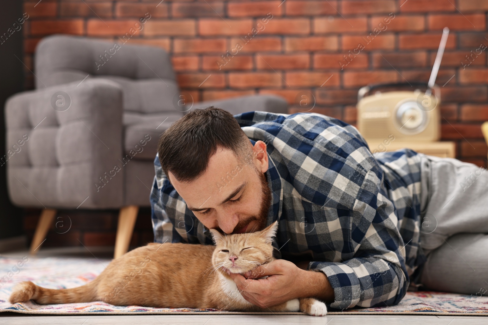 Photo of Man petting cute ginger cat on floor at home