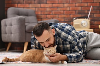 Man petting cute ginger cat on floor at home