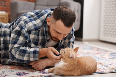 Photo of Man petting cute ginger cat on floor at home