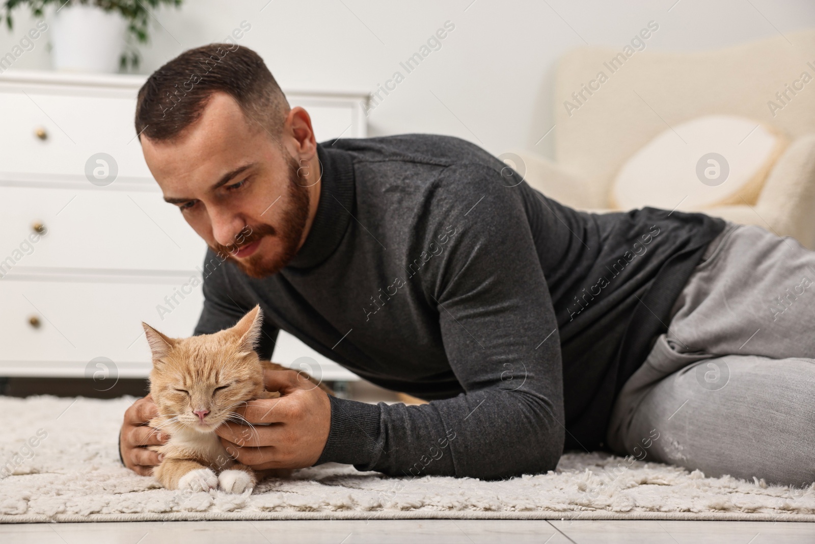 Photo of Man petting cute ginger cat on floor at home