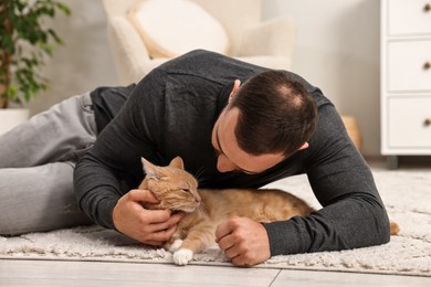 Man petting cute ginger cat on floor at home