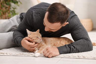 Photo of Man petting cute ginger cat on floor at home