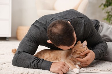 Man petting cute ginger cat on floor at home