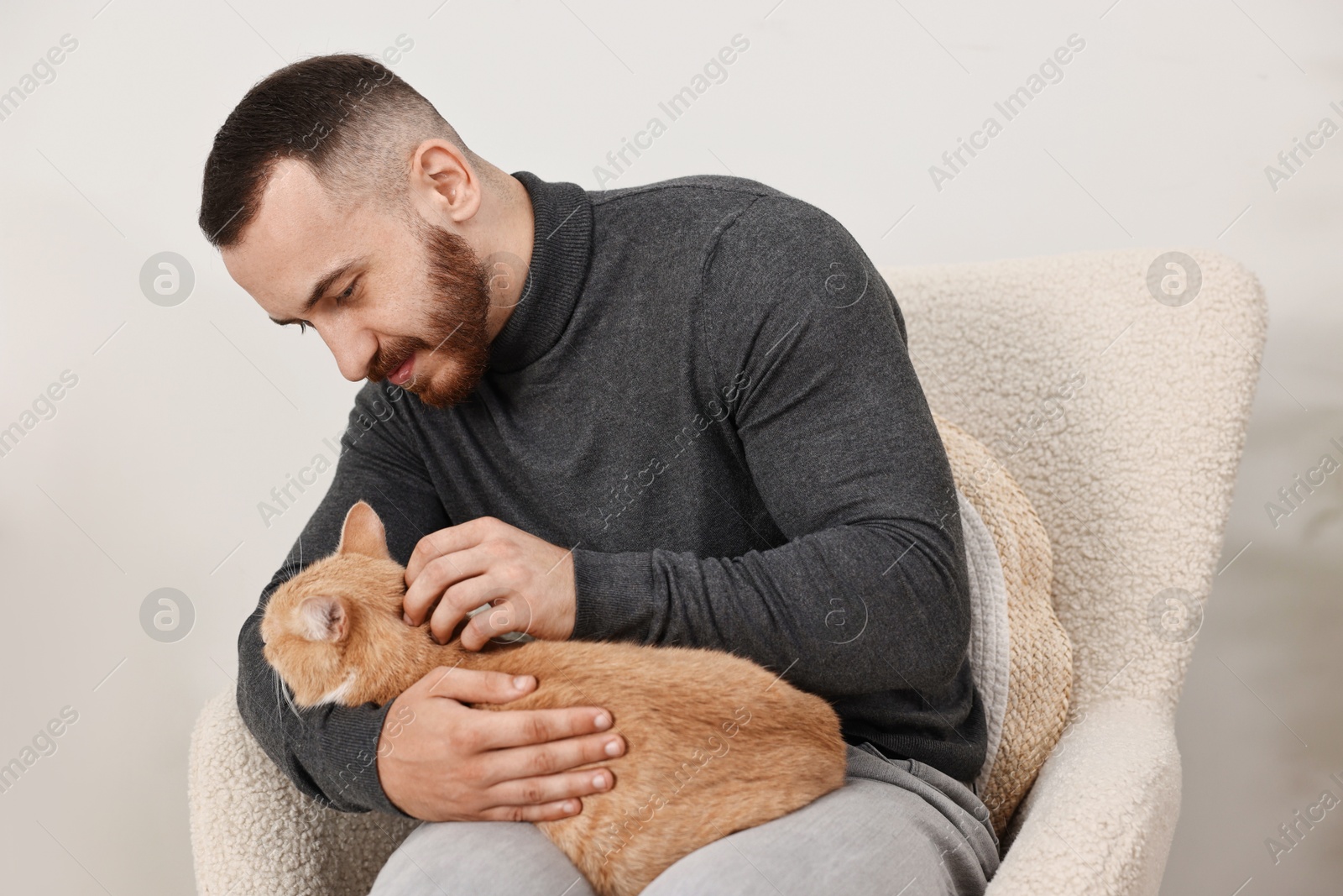 Photo of Man petting cute ginger cat on armchair at home