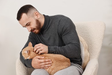 Photo of Man petting cute ginger cat on armchair at home