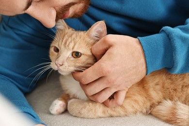 Photo of Man petting cute ginger cat on sofa at home, closeup