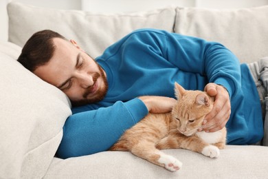 Man petting cute ginger cat on sofa at home