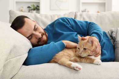 Man petting cute ginger cat on sofa at home