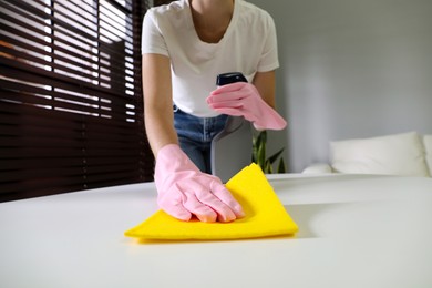 Young woman cleaning table with rag and spray in office, closeup