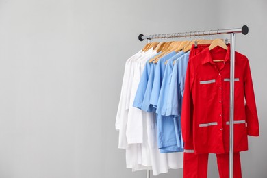 Photo of Different medical workers' uniforms on clothing rack against grey background. Space for text