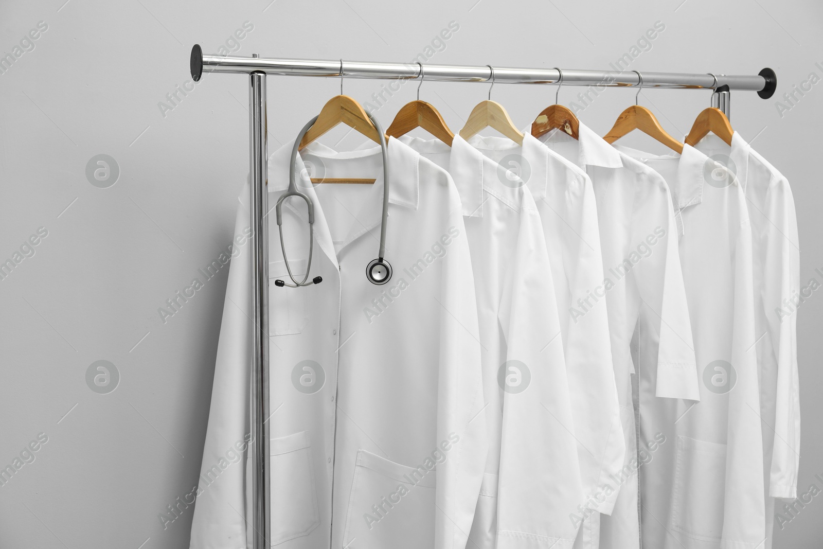 Photo of Different medical workers' uniforms and stethoscope on clothing rack against grey background